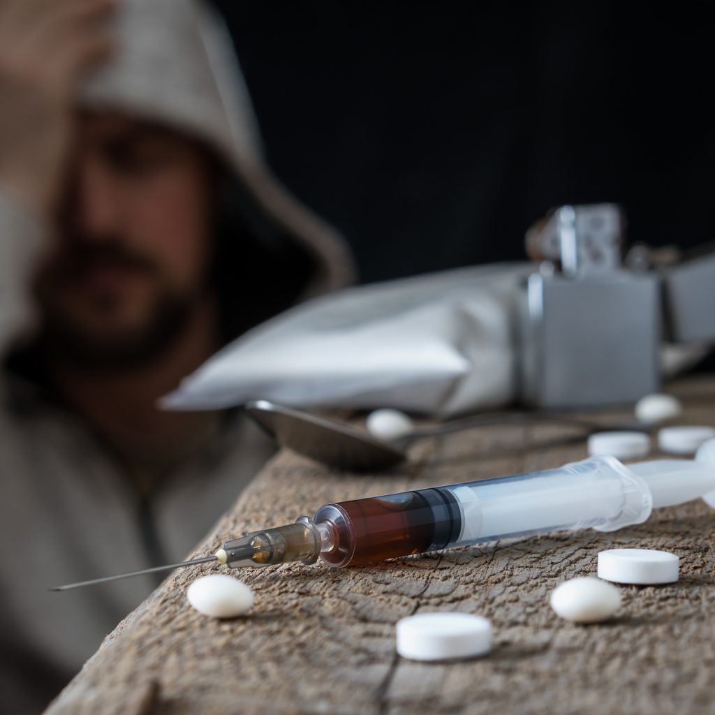 Drugs concept. Depressed young man sitting after using different types of drugs, drug overdose.